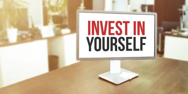 Monitor in modern office with INVEST IN YOURSELF text on the screen.