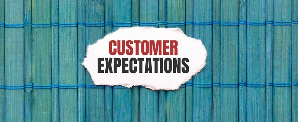 CUSTOMER EXPECTATIONS text on the piece of paper on the green wood background