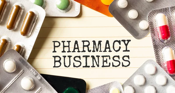 Text PHARMACY BUSINESS on a white background. Nearby are various medicines. Medical concept