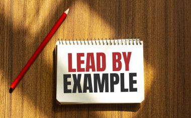 Beyaz arkaplanda örnekle öncülük eden kırmızı kalem ve not defteri