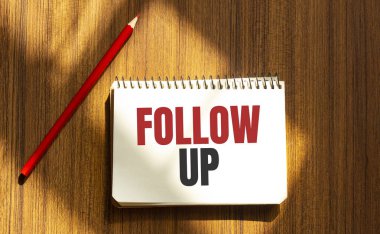 Beyaz arkaplanda FOLLOW UP yazısıyla kırmızı kalem ve not defteri