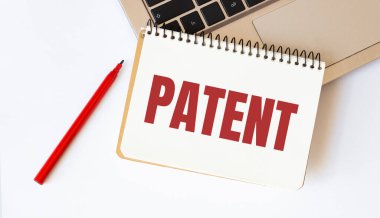 Dizüstü bilgisayar, kırmızı kalem ve beyaz arka planda metin patentli not defteri