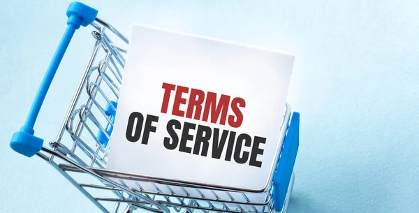 Shopping cart and text TERMS OF SERVICE on white paper note list. Shopping list concept on blue background.