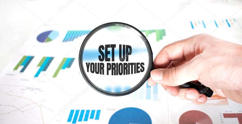 Magnifying glass with words SET UP YOUR PRIORITIES over wooden background. Business concept.