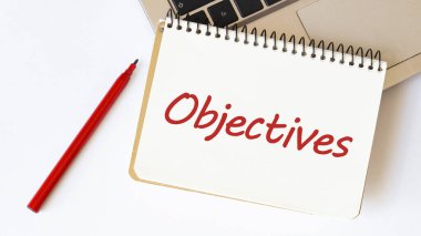 Laptop, kırmızı kalem ve beyaz arkaplanda OBJECTIVES yazılı not defteri