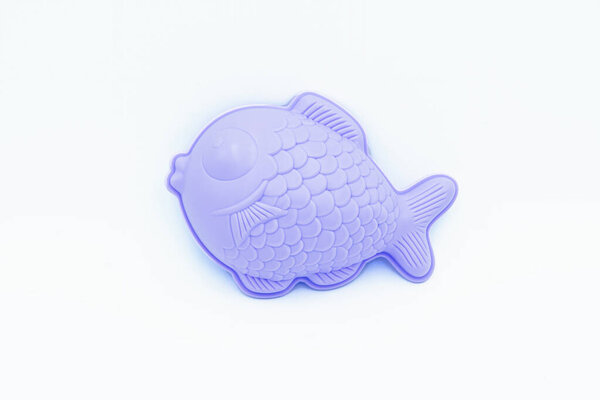 Beach toys: a purple fish shaped sand mold on a white background