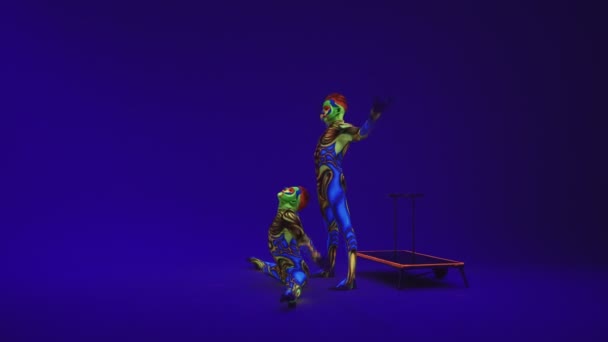 Jumeaux acrobatiques en costumes néon pour effectuer un stand sur les mains et la tête, sur cyclorama bleu en maquillage ultraviolet dans un style extraterrestre..