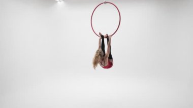 Kırmızı elbiseli, siyah çoraplı esnek sarışın kız hava çemberinde akrobatik elementler sergiliyor..