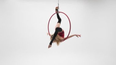 Kırmızı elbiseli, siyah çoraplı esnek sarışın kız hava çemberinde akrobatik elementler sergiliyor..