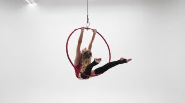 Kırmızı elbiseli, siyah çoraplı esnek sarışın kız hava çemberinde akrobatik elementler sergiliyor..