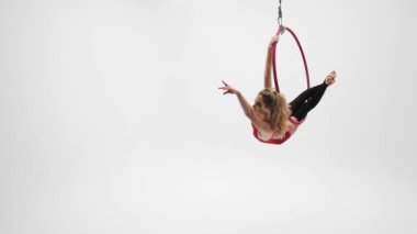 Kırmızı elbiseli, siyah çoraplı esnek sarışın kız hava çemberinde akrobatik elementler sergiliyor..