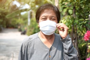 Tayland 'da Covid-19 ya da Corona virüsünü önlemek ve Hava Kirliliği Değeri 2,5 PM' yi korumak için beyaz bez maskeli yaşlı bir Asyalı kadın. Bahçe konseptinde yaşlıların sağlığı ve ilaçları