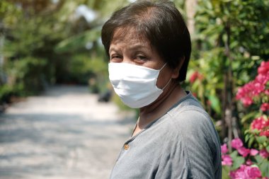 Tayland 'da Covid-19 ya da Corona virüsünü önlemek ve Hava Kirliliği Değeri 2,5 PM' yi korumak için beyaz bez maskeli yaşlı bir Asyalı kadın. Bahçe konseptinde yaşlıların sağlığı ve ilaçları