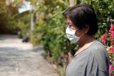 Tayland 'da Covid-19 veya Corona virüsünü önlemek ve Hava Kirliliği Değeri 2,5 Pm' yi korumak için gözlük ve beyaz bez maske takan Asyalı yaşlı kadın. Bahçe konseptinde yaşlıların sağlığı ve ilaçları