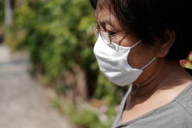 Tayland 'da Covid-19 veya Corona virüsünü önlemek ve Hava Kirliliği Değeri 2,5 Pm' yi korumak için gözlük ve beyaz bez maske takan Asyalı yaşlı kadın. Bahçe konseptinde yaşlıların sağlığı ve ilaçları
