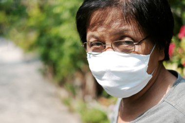 Tayland 'da Covid-19 veya Corona virüsünü önlemek ve Hava Kirliliği Değeri 2,5 Pm' yi korumak için gözlük ve beyaz bez maske takan Asyalı yaşlı kadın. Bahçe konseptinde yaşlıların sağlığı ve ilaçları