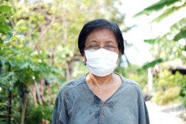Tayland 'da Covid-19 veya Corona virüsünü önlemek ve Hava Kirliliği Değeri 2,5 Pm' yi korumak için Asyalı yaşlı kadın bahçıvan terliyor ve beyaz bez maskeli gözlük takıyor. Sağlık Yaşlıları Konsepti.