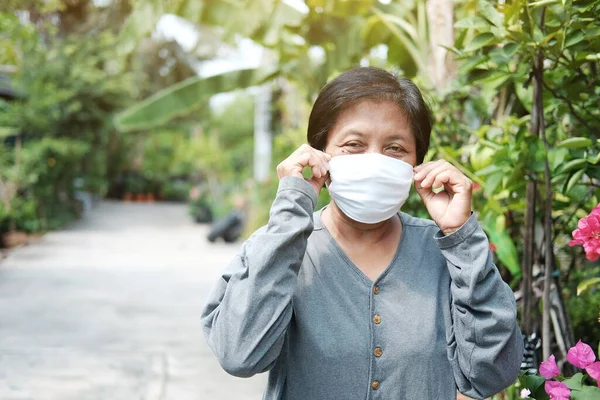 Asian old woman wearing a white cloth mask for prevent the Covid-19 or Corona virus in Thailand and protection for Air Pollution Value Pm 2.5. Health and medicine of elderly in garden concept