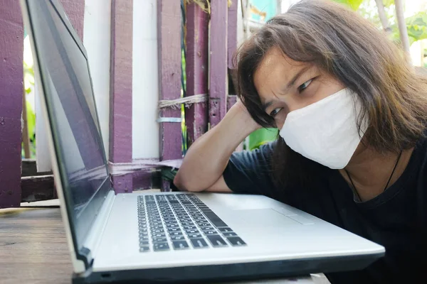 Asian Thai woman wearing a white cloth mask for prevent the Covid-19 or Corona virus and she serious work from home with laptop and problem working online system. Air Pollution Value Pm 2.5 concept.