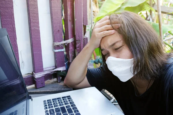 Asian Thai woman wearing a white cloth mask for prevent the Covid-19 or Corona virus and she serious work from home with laptop and problem working online system. Air Pollution Value Pm 2.5 concept.