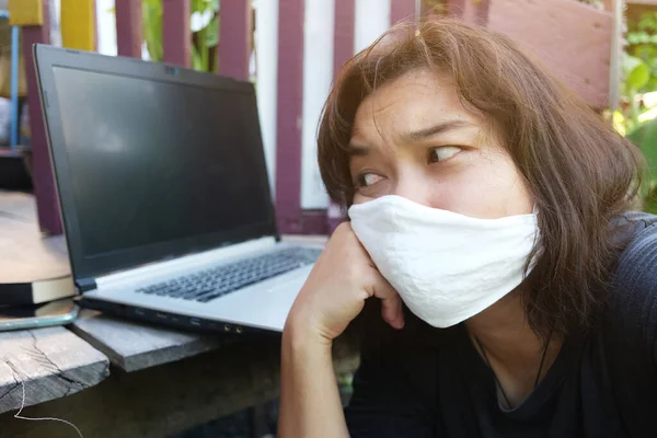 Asian Thai woman wearing a white cloth mask for prevent the Covid-19 or Corona virus and she serious work from home with laptop and problem working online system. Air Pollution Value Pm 2.5 concept.