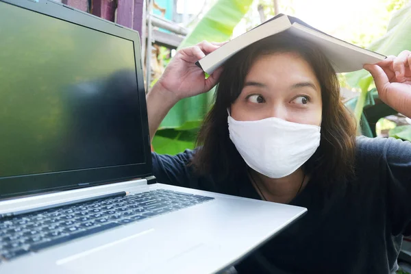 Covid 19やコロナウイルスを防ぐために白い布マスクをしているアジア系タイ人女性は ノートパソコンのオンラインシステムを使って自宅から仕事のための本を真剣に読んでいます 大気汚染値Pm 5の概念 — ストック写真