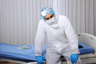 Hasta yatağında oturan Şahsi Koruyucu Ekipman veya PPE giysisi giyen bir tıp adamı. Bu yüzden Covid 19 virüsü kapıp Tayland 'daki hastanede tedavi görenlere şifa vermeye çalıştı.
