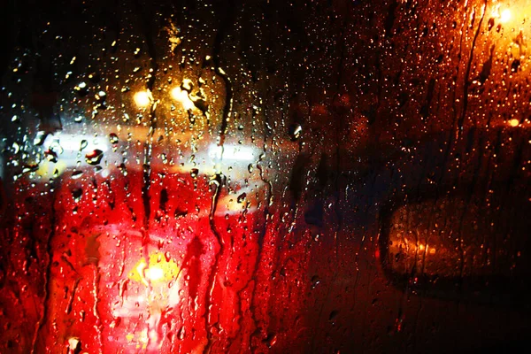 雨が降る雨が窓ガラスに質感を落とし 光の抽象的なぼやけた街並みが広がっています ソフトフォーカス — ストック写真