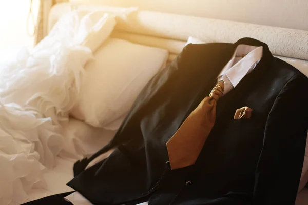 ウェディングドレスとスーツは ホテルの部屋で美しい太陽の光と白いベッドの上に横たわっています バレンタインデーとお祝いのコンセプトへの愛 — ストック写真