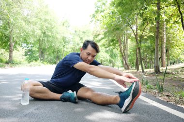 Gülümseyen Asyalı adam çimento zeminde koşup bahçede koştuktan sonra kasları gevşetmek için egzersiz yapıyor ve bacaklarını esnetiyordu. Spor ve sağlıklı kavram