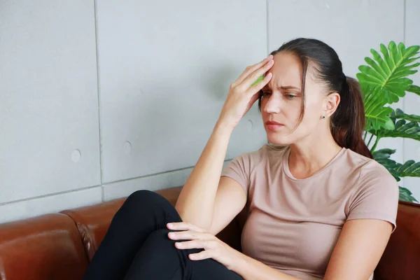 Young Caucasian woman is suffering from depression and headache on brown sofa and stressed with having problems in society.