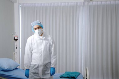 Kişisel Koruyucu Ekipman ya da PPE kumaş bölümünde çalışan beyaz bir doktor. Hastanenin acil servisinde hasta yatağının yanında durmaya çalış.