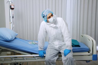 Kişisel Koruyucu Ekipman ya da PPE kumaş bölümünde çalışan beyaz bir doktor. Hastanenin acil servisindeki hasta yatağında aşırı yüklenme var.