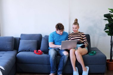 Smiling Young Caucasian couple love relaxing with laptop in social media for shopping online in living room. Technology for Married family lifestyle on holiday Concept. clipart