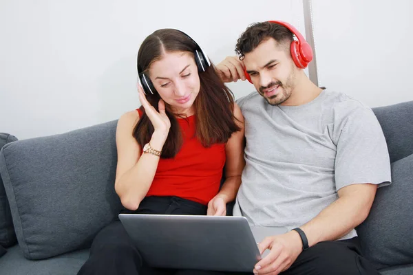 Gülümseyen beyaz bir çift, oturma odasında birlikte kulaklık ve dizüstü bilgisayarla çevrimiçi müzik dinledikleri için zevk alıyorlar. Tatilde evlilik hayatı ve yaşam tarzı kavramı.