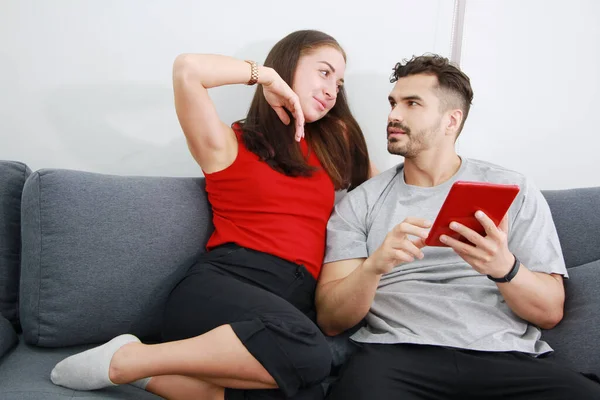 Gülümseyen beyaz çift göz teması kuruyor ve internette sosyal medya teknolojilerinde dizüstü bilgisayarla oturma odasındaki kanepede eğleniyorlar. Tatilde evde çalışmak ve evli aile hayatı..