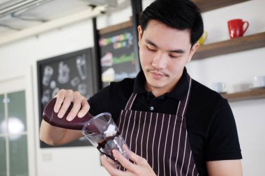 Gülümseyen Asyalı barmen taze çikolata sanatını bir bardak Cappuccino buzlu kahvesine dolduruyor..
