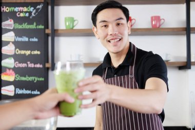Gülümseyen Asyalı barista genç adam plastik bir bardak kibrit yeşil çay servisi yapıyor ve kahve dükkanındaki tezgahtaki müşteriler için eve götürüyor. İşçilik için çalıştırma kavramı