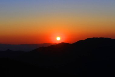 Gökyüzünde ve bulutta gün batımı, güzel rengarenk alacakaranlık zamanı dağ siluetiyle.