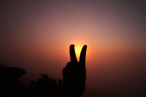 Beautiful silhouette of Female hand raised up with two lifted fingers in natural sunrise and sunset for encourage herself
