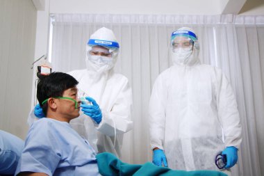 Kişisel Koruyucu Ekip ya da PPE giysileri ve Asyalı yaşlı hasta için solunum cihazı kullanan profesyonel tıbbi ekip, Covid 19 virüsü bulaşmış solunum sistemidir..