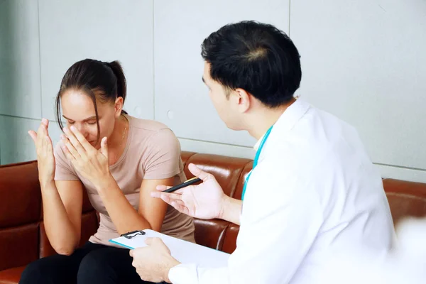 Young asian male psychiatrist is specialist in psychiatry is talking with Caucasian female Patient is headache and encouraging to her in Clinical treatment for emotional symptoms. focus at a woman.
