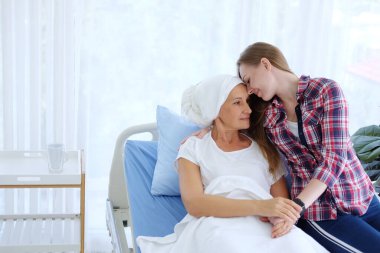 Beyaz başörtülü Kafkasyalı Yaşlı Anne kemoterapiden sonra yatakta yatıyor çünkü kanser ya da lösemi hastası ve küçük kızı annesine sarılıp ona bakıyor..