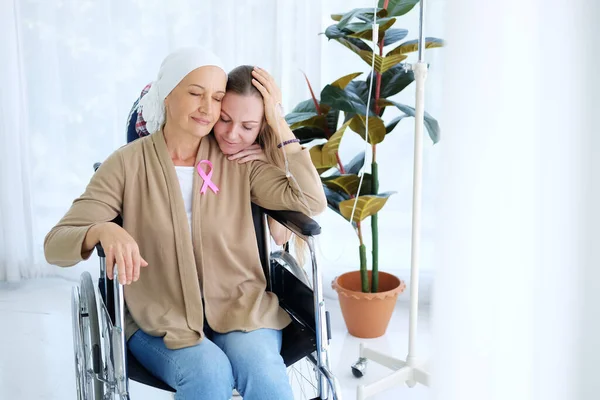 Beyaz başörtüsü takmış annesine sevgi ve özenle sarılan beyaz kız kemoterapiden sonra tekerlekli sandalyede oturuyor. Yaşlı anne kanser ya da lösemi hastası..