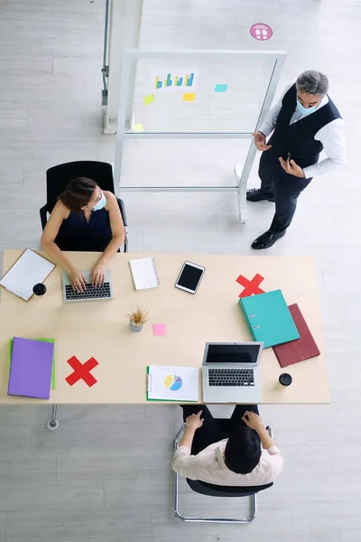 Asian team and Caucasian boss is businesspeople teamwork wearing mask for preventing covid19 virus and brainstorming in meeting room at office. Healthcare and New normal lifestyle in business concept.