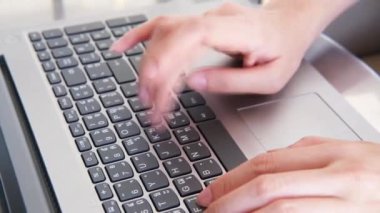 Kadın elinin kapalı olduğu yerde Tayland alfabesi ve dizüstü bilgisayar klavyesinde İngilizce alfabesi yazıyor.