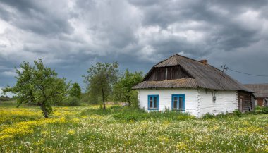 Çamurla kaplanmış eski ahşap bir kır evi ve çiçek açan çayırların arasında beyaz kille boyanmış..