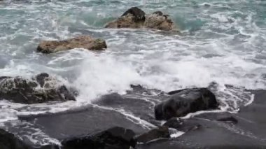 Deniz dalgaları kayalardan oluşan karanlık kayalara çarpar. Köpüklü sörf.