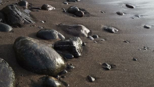 黒い石と暗い砂に対して実行される海の波 — ストック動画