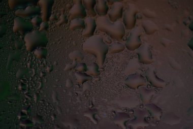 Şehir ışıklarıyla ıslak pencere camına su damlıyor.